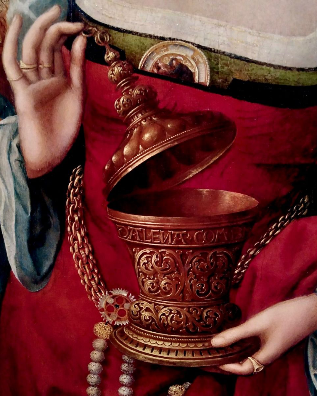 Detalle pictórico de unas manos sosteniendo un ungüentario dorado